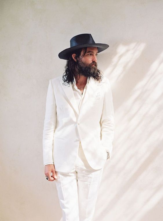 a boho groom's look with a white suit, a white shirt and a black hat is a gorgeous solution to rock