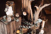 a boho wedding decoration of crates with candle lanterns, pampas grass and greenery and blooms