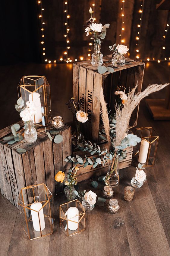 a boho wedding decoration of crates with candle lanterns, pampas grass and greenery and blooms