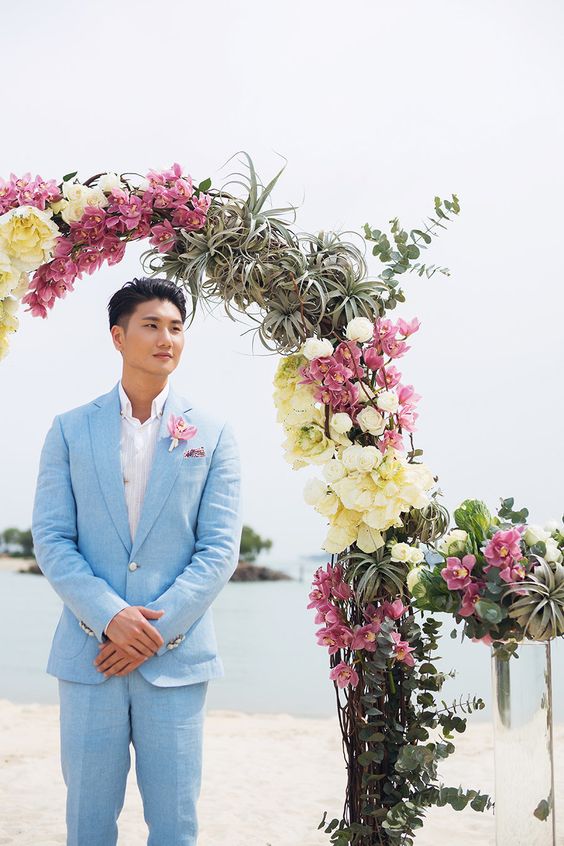 a catchy tropical groom's look with a light blue suit, a white shirt and a bold boutonniere is amazing for summer