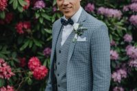 a checked blue three-piece suit, a white shirt, a navy polka dot bow tie plus a white floral boutonniere