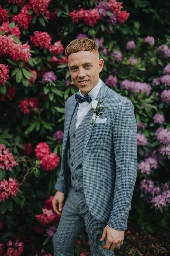 A checked blue three piece suit, a white shirt, a navy polka dot bow tie plus a white floral boutonniere