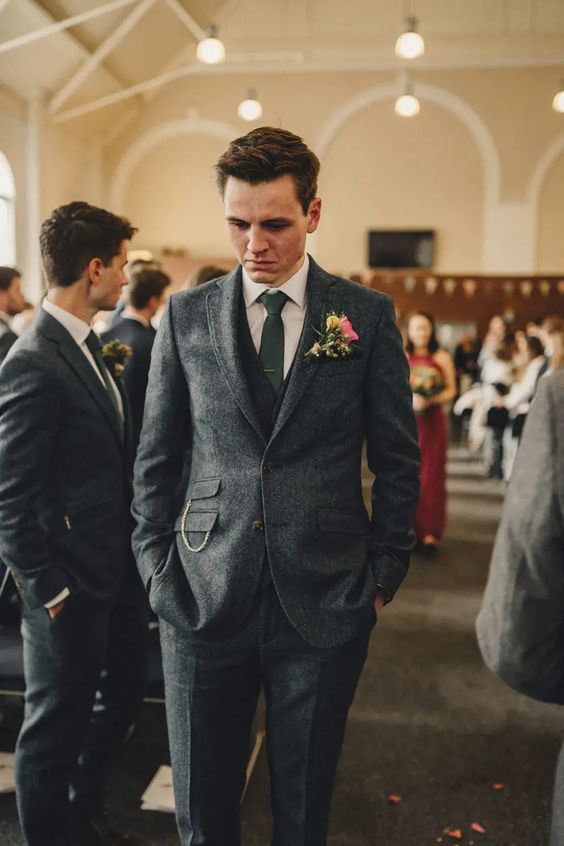 a chic grey groom's outfit with a white shirt, a green tie, a chain and a bright flower boutonniere