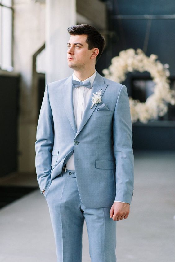 a chic groom's look with a light blue suit, a white shirt, a light blue bow tie and a boutonniere is amazing