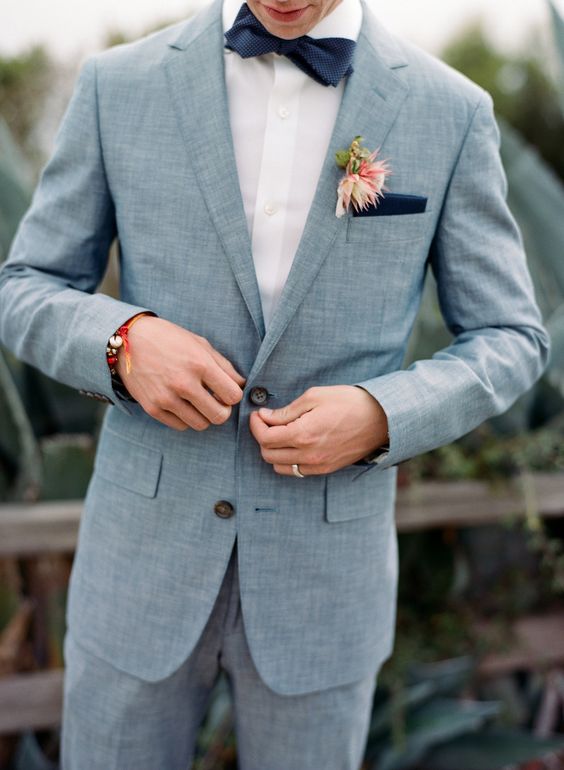 a chic light blue suit, a white shirt, a navy bow tie and a handkerchief plus a floral boutonniere