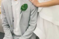 a chic minimalist groom’s outfit wiht a dove grey pantsuit, a white shirt and a green leaf boutonniere for a tropical wedding