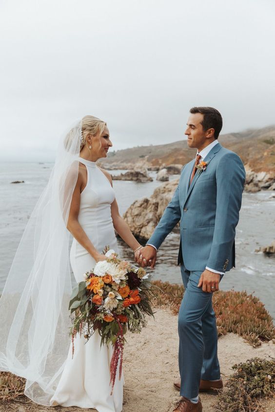 a coastal groom's look with a blue suit, a white shirt, a rust tie, borwn shoes and a bold boutonniere is amazing for the fall