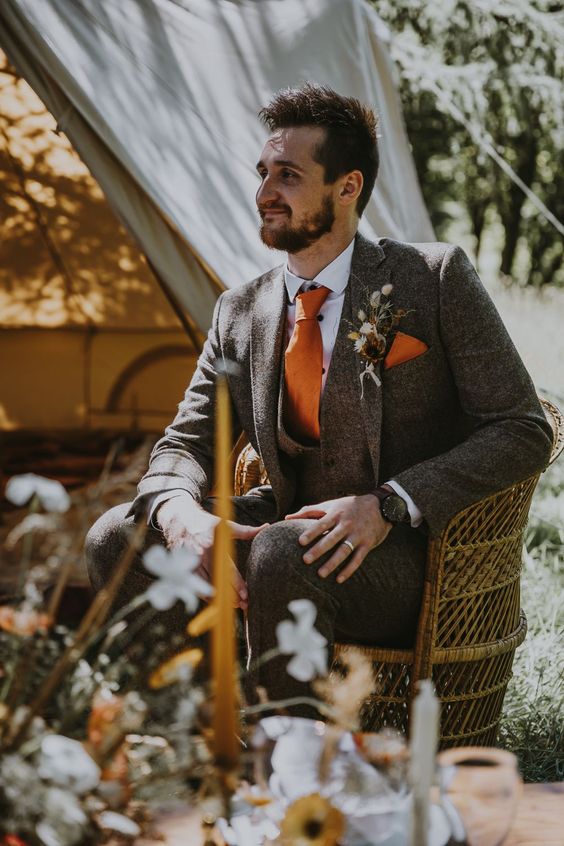 a cool boho groom's look with a grey three-piece suit, a white shirt, an orange tie and a handkerchief plus a dried flower boutonniere