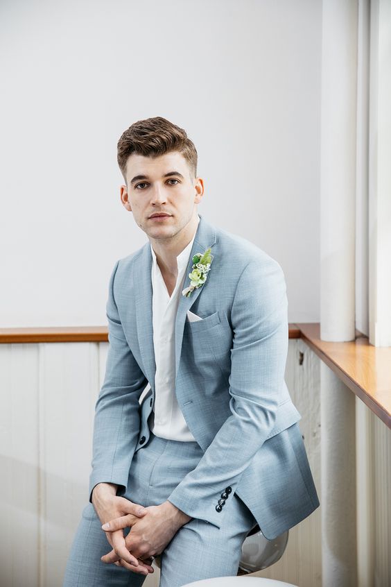 a delicate blue grey suit, a white shirt with no tie, a boutonniere for a relaxed and effortlessly chic look