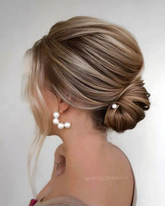 A dimensional low chignon with a volume on top and some face framing locks is adorable