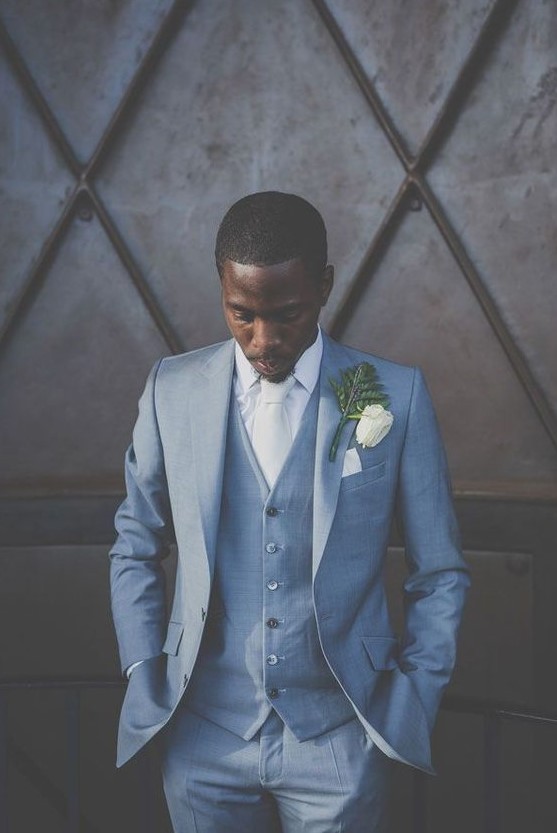 A formal groom's look with a blue three piece suit, a white shirt and a tie plus a whimsical boutonniere