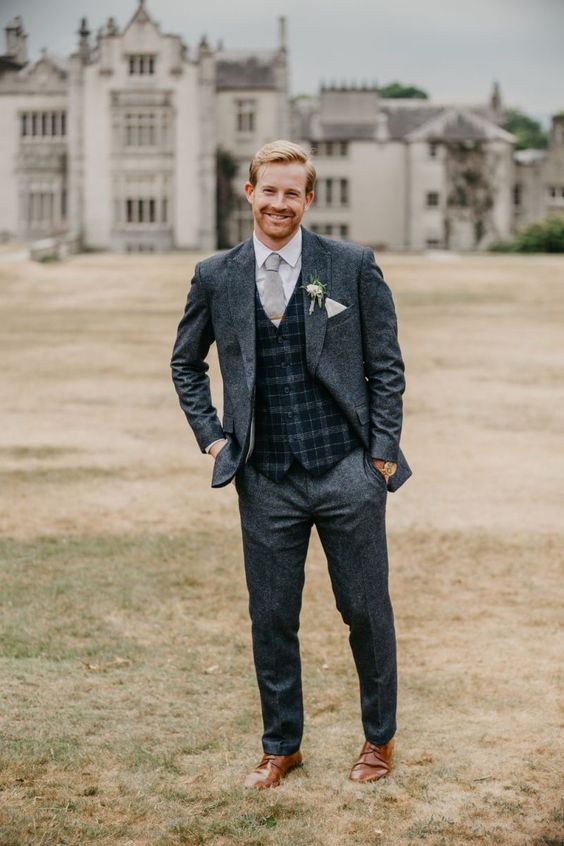 a graphite grey suit, a navy plaid waistcoat, brown shoes and a dove grey tie plus a white flower boutonniere