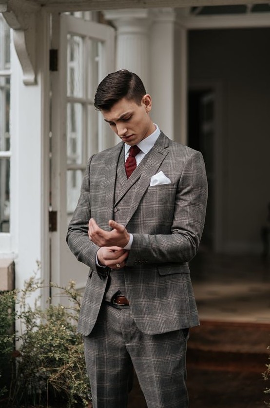 a grey checked three-piece suit, a white shirt, a burgundy bow tie and a brown belt for a touch of vintage