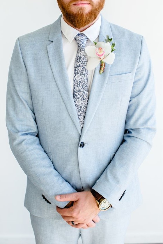 a light blue wedding suit, a white shirt and a blue floral print tie plus an orchid boutonniere for a tropical groom