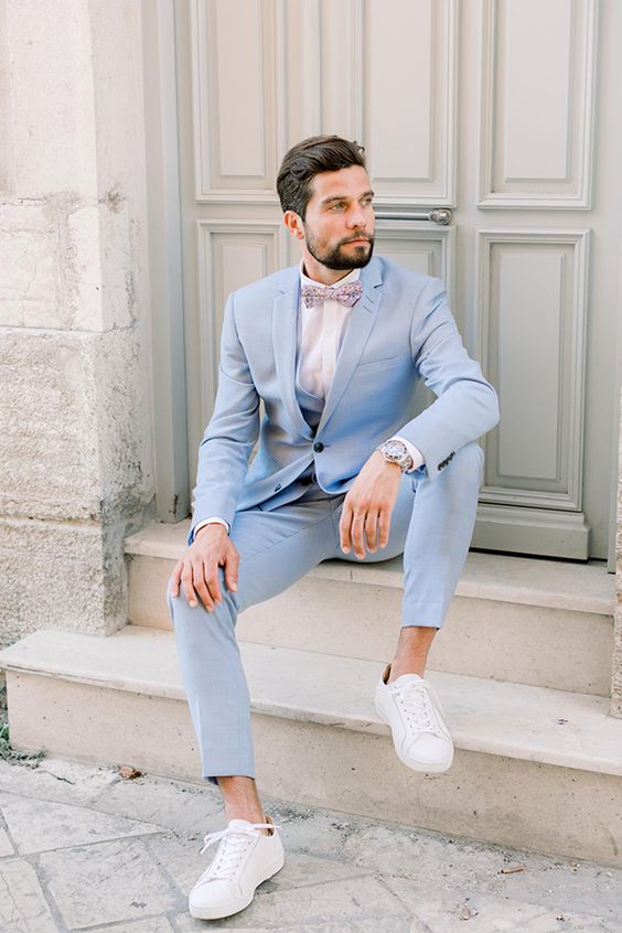 A lovely pale blue three piece pantsuit, a white shirt, a printed bow tie, white sneakers and a watch compose a cool look for summer