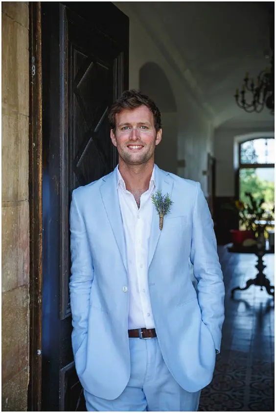 a lovely spring or summer groom's look with a pale blue suit, a white shirt, a greenery boutonniere for relaxed elegance