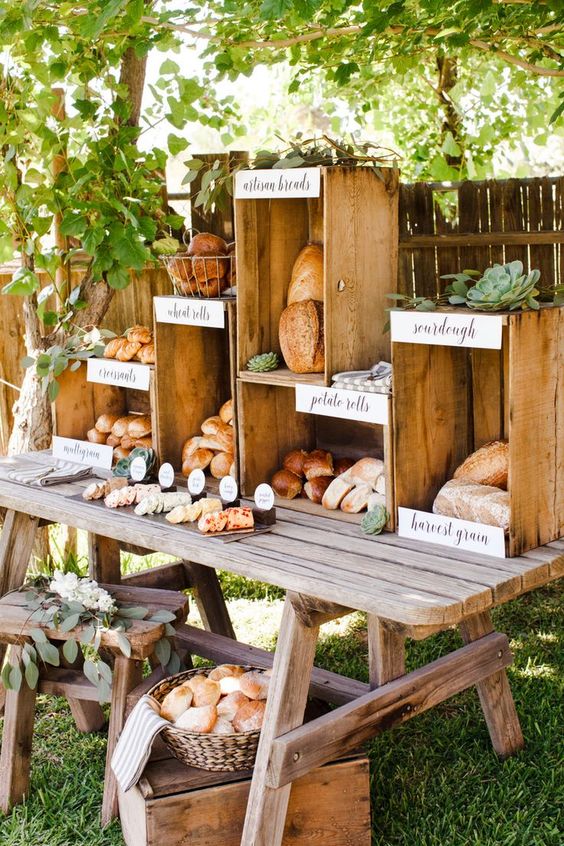 a lovely wedding food station with crates and a wooden table, some baskets, greenery, blooms and succulents is cool and pretty