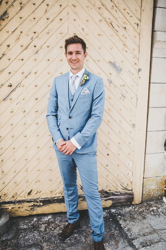 a pretty summer groom's look with a light blue three-piece suit, a white shirt, a printed tie, dark brown shoes
