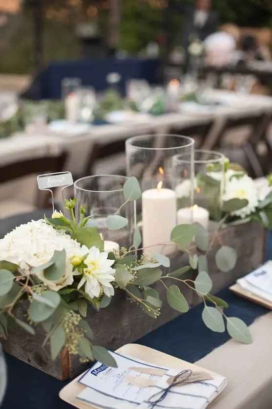 a reclaimed wooden crate with blooms, eucalyptus and candle holders is a cool rustic wedding centerpiece you can repeat yourself