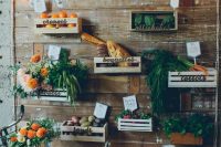 a reclaimed wooden wall with crates and various flowers, vegetables, fruits, lights and letters for a farm to table wedding