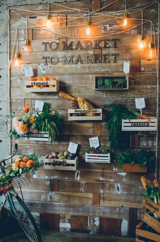 a reclaimed wooden wall with crates and various flowers, vegetables, fruits, lights and letters for a farm to table wedding
