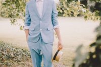 a relaxed and cool groom’s outfit with a pale blue suit, a blazer with cuffed sleeves, a white shirt, brown suede shoes and a straw bag
