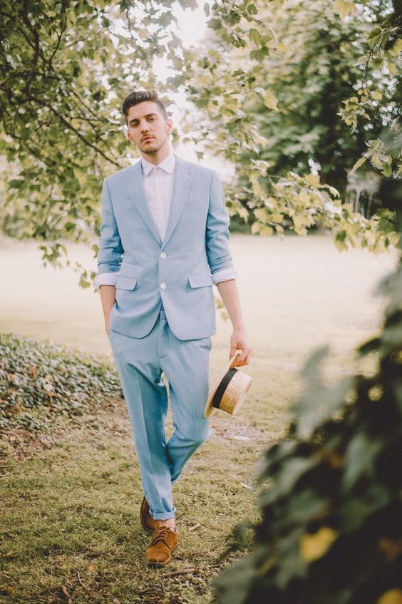 a relaxed and cool groom's outfit with a pale blue suit, a blazer with cuffed sleeves, a white shirt, brown suede shoes and a straw bag
