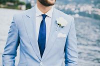 a relaxed coastal groom’s look with a pale blue suit, a white shirt, a navy tie, a white flower boutonniere is amazing