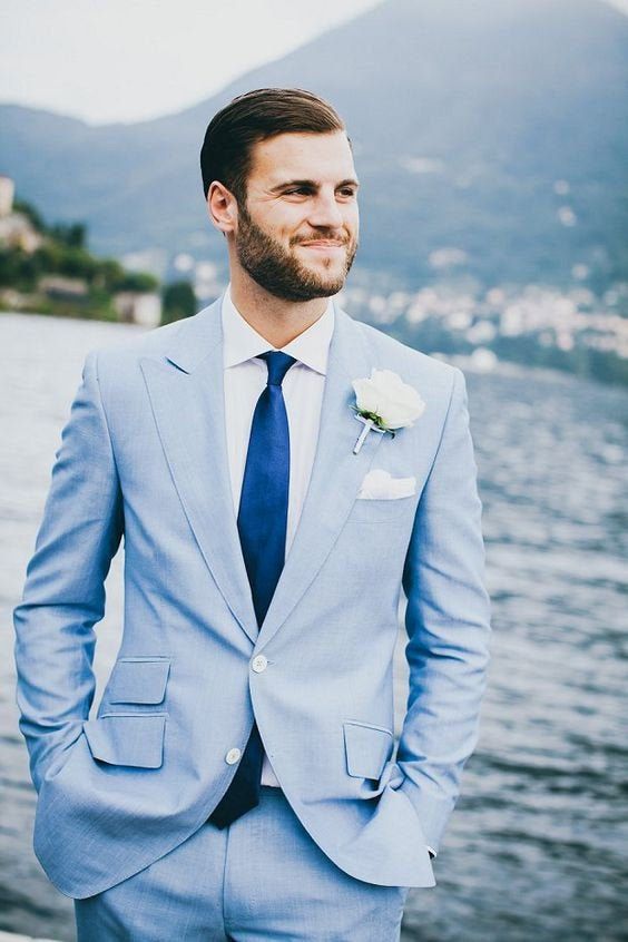 a relaxed coastal groom's look with a pale blue suit, a white shirt, a navy tie, a white flower boutonniere is amazing