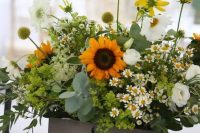 a relaxed rustic wedding centerpiece in a crate, with sunflowers, daisies, greenery, billy balls, green hydrangeas and white ranunculus is wow