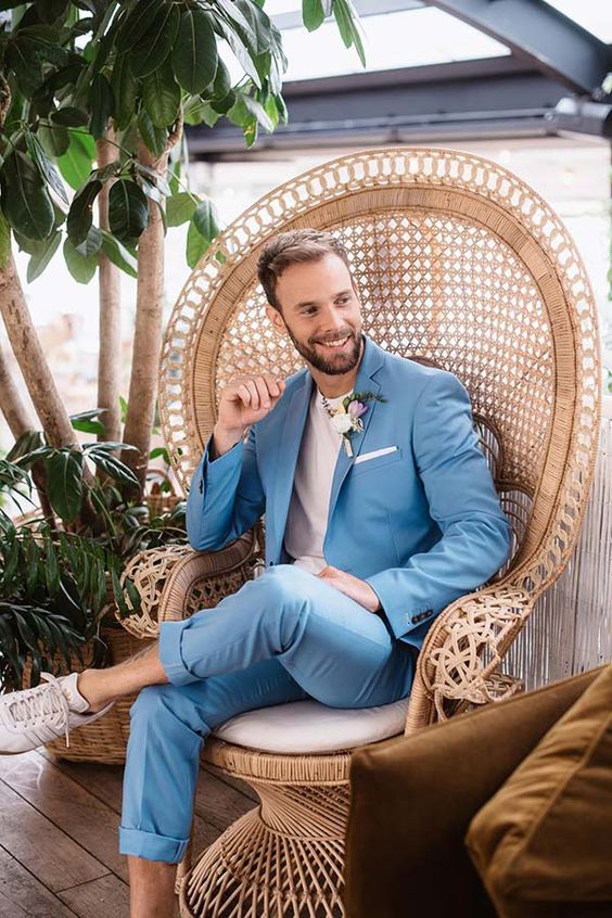 A relaxed summer groom's look with a blue suit and cuffed pants, a white t shirt, a boutonniere and white sneakers