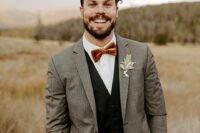 a rustic groom’s outfit with a grey blazer, a black waistcoat and pants, a white shirt and a rust velvet bow tie