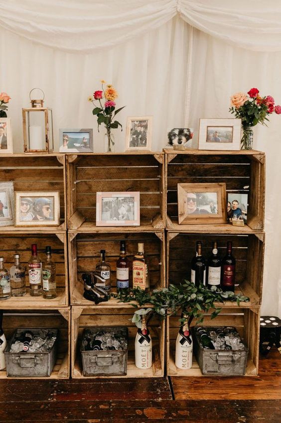 a rustic wedding bar of crates, greenery, wine and liquor bottles, family photos and blooms is super cool