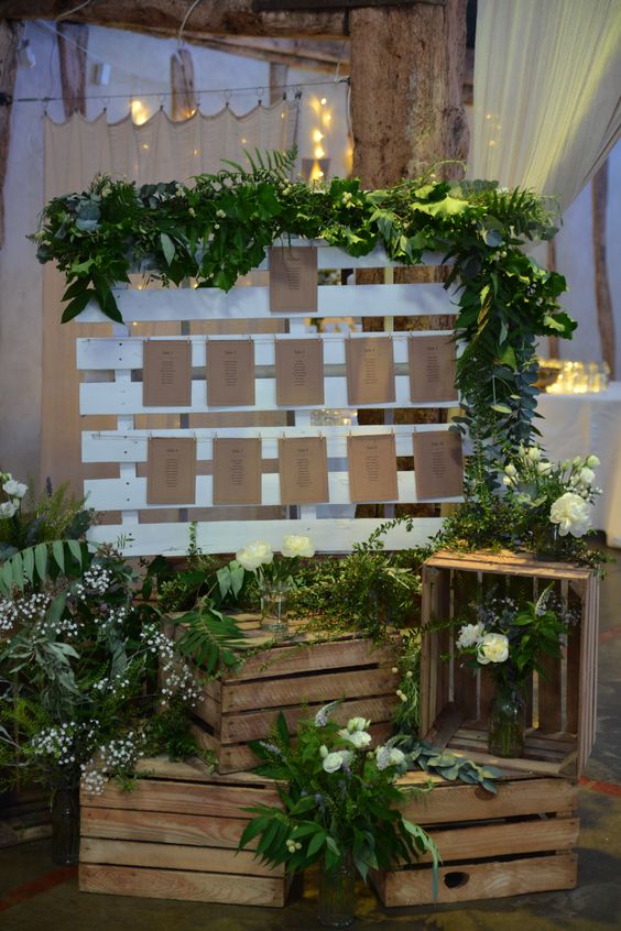 a rustic wedding seating chart decorated with greenery and with crates with greenery and white blooms