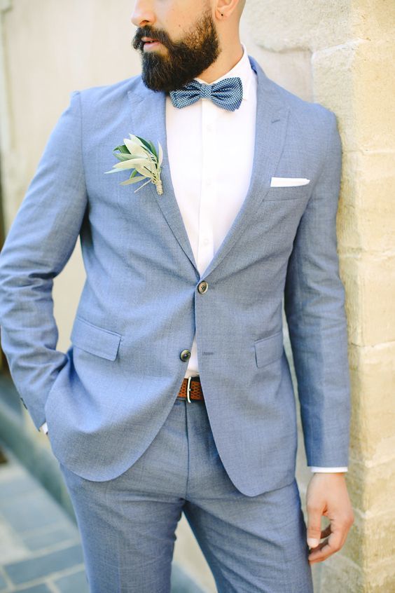 a stylish blue suit, a white shirt, a navy printed bow tie and a boutonniere are a cool combo for spring or summer