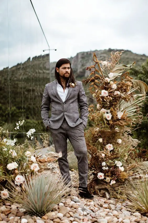 a stylish boho groom's look with a grey checked suit, a white shirt and a dried flower boutonniere is cool