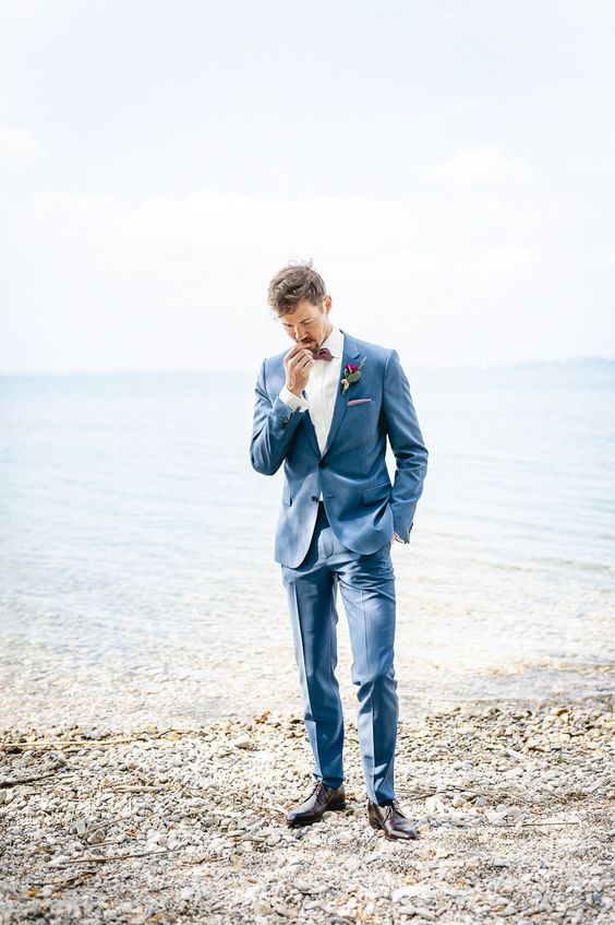 a stylish coastal groom's outfit with a blue suit, a white shirt, a burgundy bow tie, brown shoes and a boutonniere