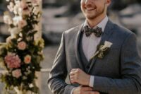 a three-piece grey pantsuit, a white shirt, a printed bow tie and a white calla boutonniere for a chic groom’s look