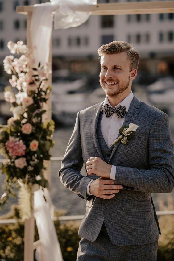 a three-piece grey pantsuit, a white shirt, a printed bow tie and a white calla boutonniere for a chic groom's look