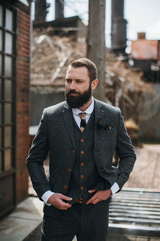 a vintage groom outfit with a grey tweed three-piece suit with copper buttons, a white shirt, a moody floral tie