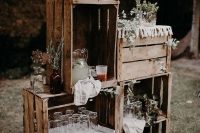 a wedding decoration or food station made of crates, with greenery and blooms, macrame, lemonade and some fruit