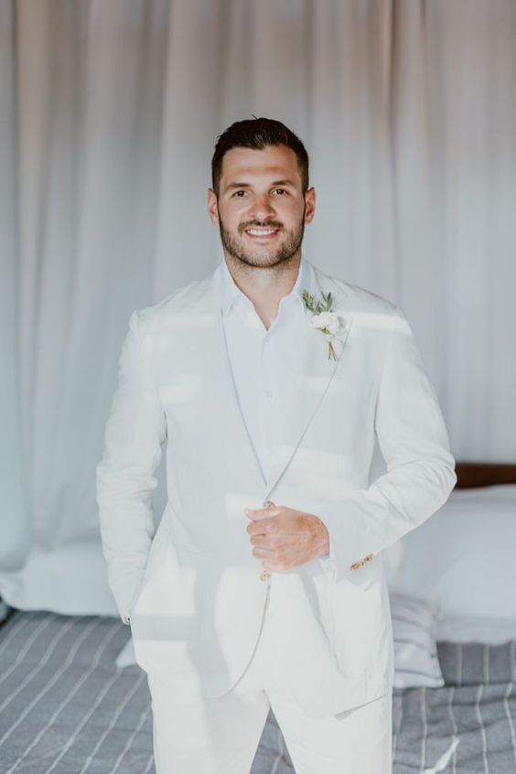 a white groom's look with a suit, a white shirt and a boutonniere is a great idea for spring or summer