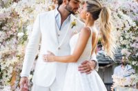 a white three-piece suit, a white shirt and a boutonniere are a super elegant and chic groom’s outfit