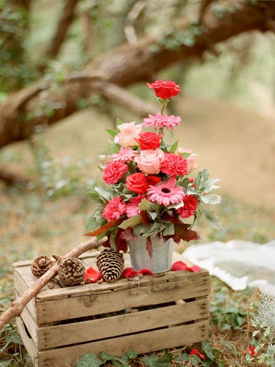 a woodland wedding decoration of a crate, pinecones, branches and a bold floral arrangement