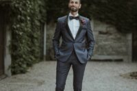 an elegant grey groom’s tuxedo with black lapels, black shoes and a black bow tie plus a bold boutonniere