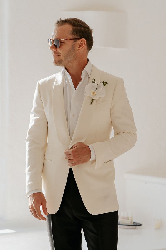 an elegant groom's look with a white shirt, a white tux and black pants plus an orchid boutonniere for a tropical wedding