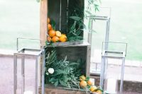 wedding venue decor with crates filled with greenery and iranges, large candle lanterns around