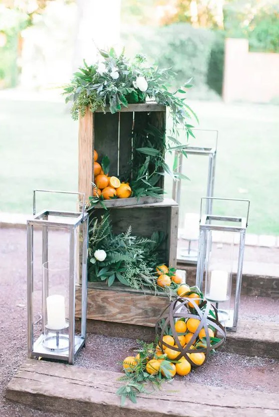 wedding venue decor with crates filled with greenery and iranges, large candle lanterns around