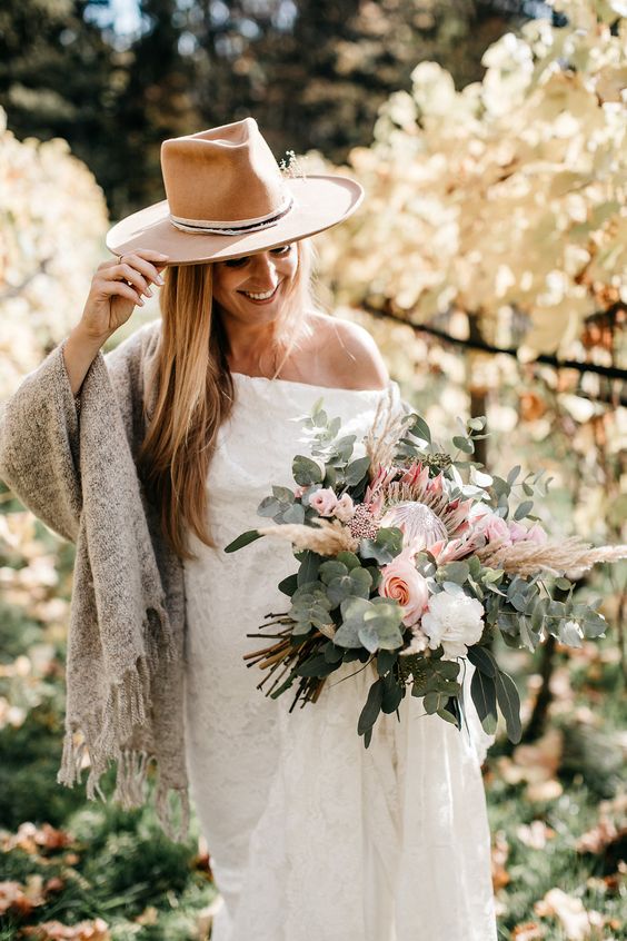 a boho bridal look with a one shoulder wedding dress, a grey coverup and a beige hat