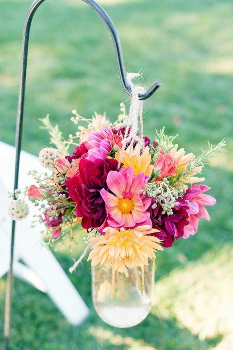 a bright floral arrangement in burgundy, pink  and yellow wth herbs in a mason jar